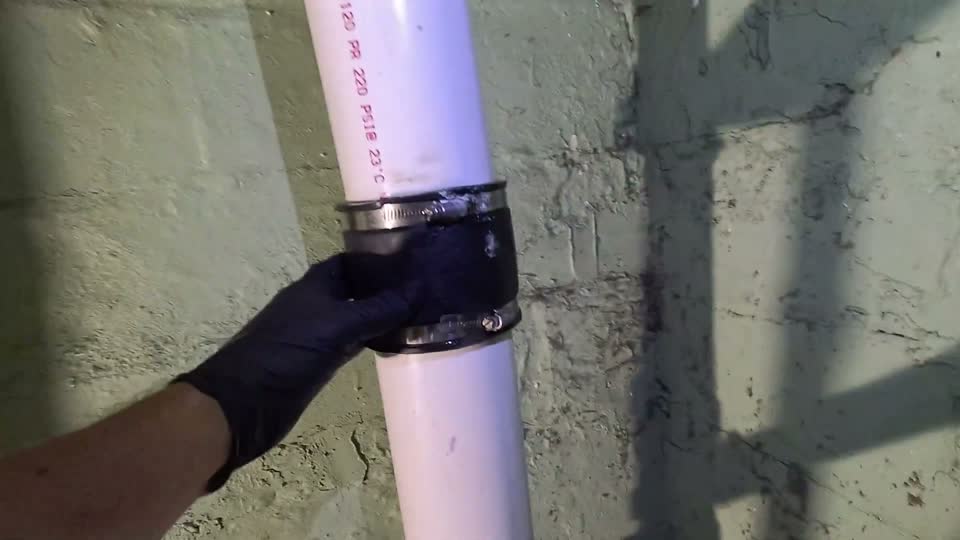 New white PVC drain stack with a sealed black coupling, photographed in a Cleveland basement